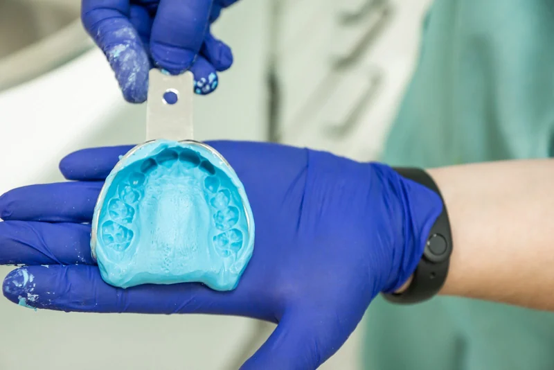 A denturist holding a dental model of teeth in a warm clinic setting